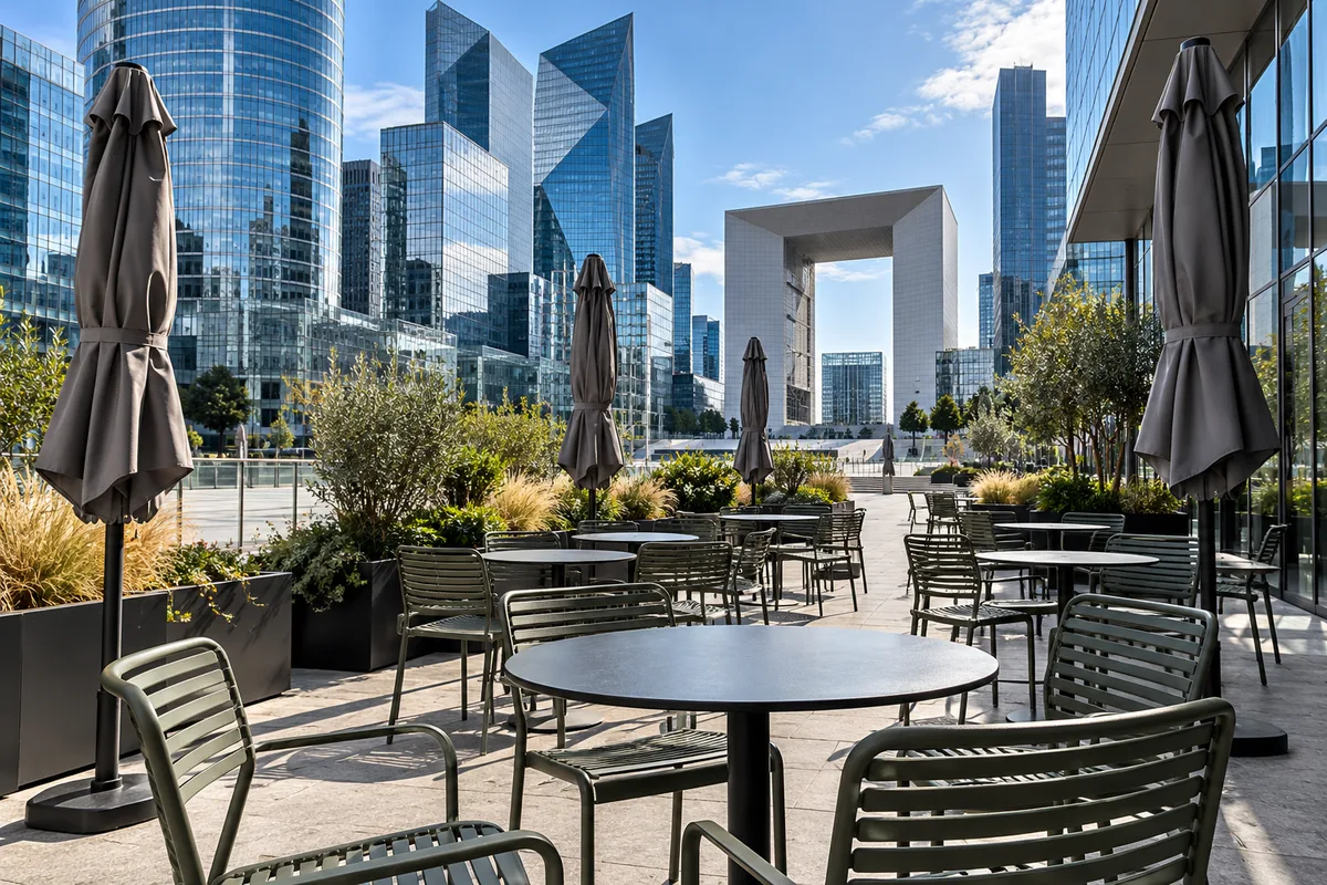 Terrasse de restaurant au pied de tours de bureaux, chaises vides et parasols repliés
